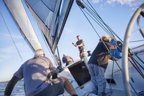 Men sailing adjusting rigging and sail on sailboat stock photo