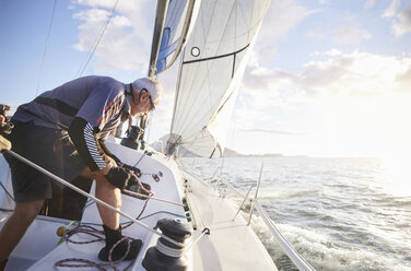 Man sailing pulling rigging on sailboat on sunny ocean - CAIF10191