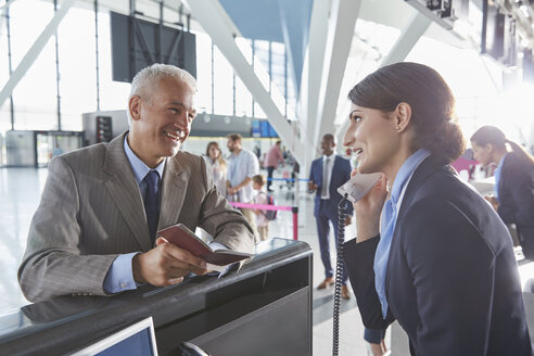 Kundendienstmitarbeiter, der einem Geschäftsmann am Check-in-Schalter des Flughafens beim Ausfüllen seines Reisepasses hilft - CAIF10193