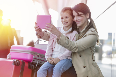 Mutter und Tochter machen ein Selfie mit einer digitalen Tablet-Kamera am Flughafen, lizenzfreies Stockfoto
