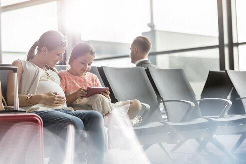 Schwangere Mutter und Tochter benutzen ein digitales Tablet im Abflugbereich eines Flughafens - CAIF10203