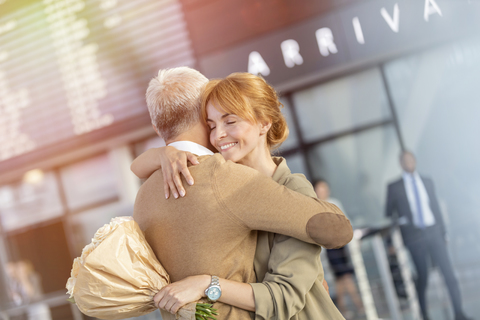 Mann und Frau mit Blumen begrüßen und umarmen im Flughafen, lizenzfreies Stockfoto