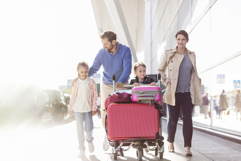 Family with luggage cart walking outside airport stock photo