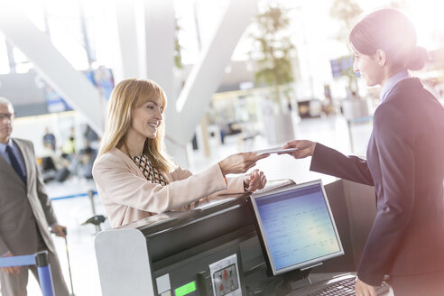 Kundendienstmitarbeiter bei der Überprüfung des Tickets einer Geschäftsfrau am Flughafen-Check-in-Schalter - CAIF10209