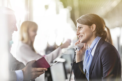 Kundendienstmitarbeiter im Telefongespräch, der einem Geschäftsmann am Flughafen-Check-in-Schalter hilft - CAIF10221