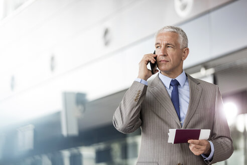 Geschäftsmann mit Reisepass und Flugticket im Gespräch mit dem Handy im Flughafen - CAIF10223