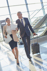 Business people discussing paperwork pulling suitcase in airport - CAIF10224