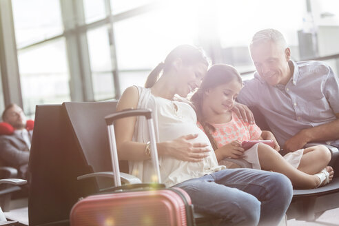 Schwangere Familie, die im Abflugbereich des Flughafens auf ein digitales Tablet wartet - CAIF10230