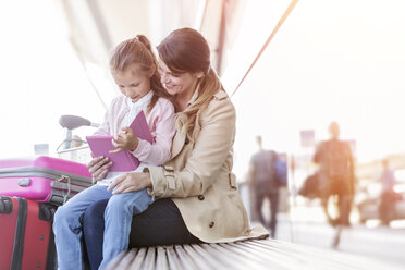 Mutter und Tochter benutzen ein digitales Tablet auf einer Bank vor dem Flughafen - CAIF10233