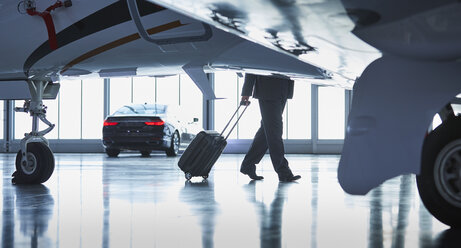 Geschäftsmann, der einen Koffer vor einem Firmenflugzeug zieht - CAIF10238