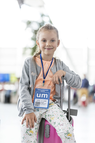 Porträt lächelnd Mädchen sitzt auf Koffer im Flughafen, lizenzfreies Stockfoto