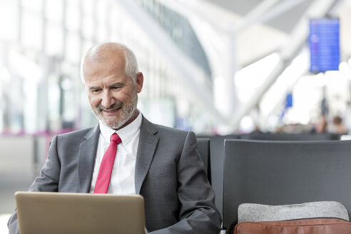 Geschäftsmann arbeitet mit Laptop im Abflugbereich des Flughafens - CAIF10259