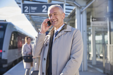 Lächelnder Geschäftsmann, der außerhalb des Flughafens mit einem Handy telefoniert - CAIF10260