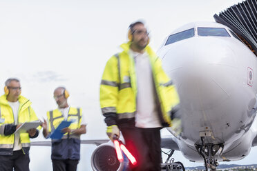 Air traffic controllers walking in front of airplane on airport tarmac - CAIF10270