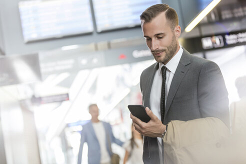 Geschäftsmann, der in einer Flughafenhalle mit seinem Mobiltelefon SMS schreibt - CAIF10271