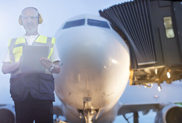 Portrait air traffic controller with clipboard in front of airplane on airport tarmac - CAIF10274