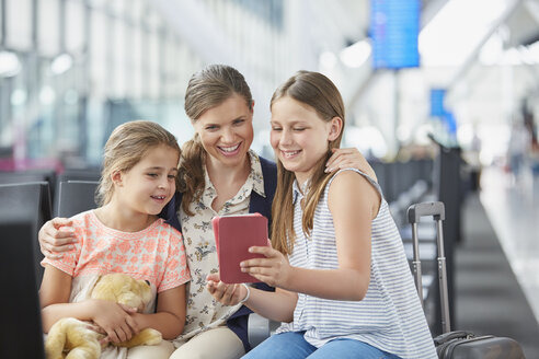 Mutter und Töchter benutzen ein digitales Tablet im Abflugbereich eines Flughafens - CAIF10281