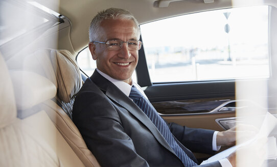 Porträt eines lächelnden Geschäftsmannes auf dem Rücksitz eines Stadtautos - CAIF10286