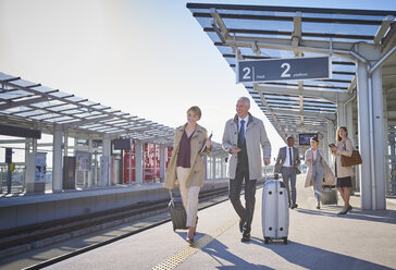 Geschäftsleute, die auf einem sonnigen Bahnhofsvorplatz mit Koffern unterwegs sind - CAIF10292