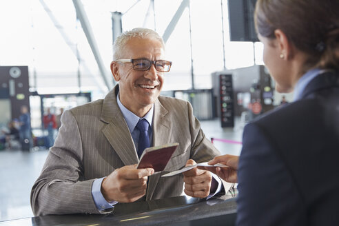 Lächelnder Geschäftsmann, der dem Kundenbetreuer am Flughafen-Check-in-Schalter seinen Reisepass übergibt - CAIF10298