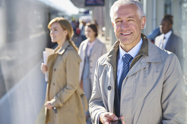 Porträt lächelnder Geschäftsmann auf sonnigem Bahnsteig - CAIF10301