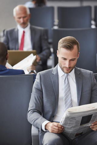 Geschäftsmann liest Zeitung beim Warten im Abflugbereich des Flughafens, lizenzfreies Stockfoto
