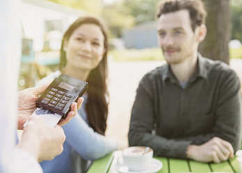 Couple watching waitress using credit card reader at outdoor cafe - CAIF10362