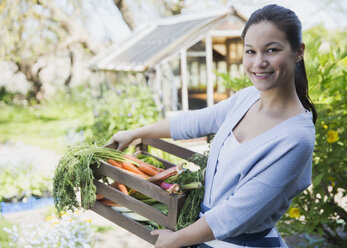 Portrait lächelnde Frau mit frisch geernteter Gemüsekiste im Garten - CAIF10365