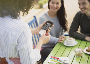 Paar beobachtet Kellnerin bei der Verwendung eines Kreditkartenlesegeräts in einem Straßencafé - CAIF10368