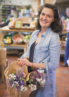Portrait lächelnde Frau mit Blumen im Korb beim Einkaufen auf dem Markt - CAIF10375