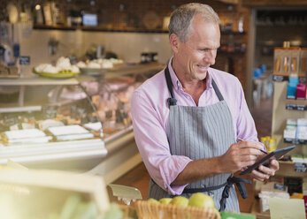 Lächelnde Angestellte eines Lebensmittelgeschäfts, die mit einem digitalen Tablet und einem Stift auf dem Markt den Bestand überprüft - CAIF10381
