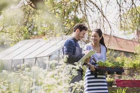 Mitarbeiter einer Gärtnerei mit Klemmbrett und Topfpflanzen im sonnigen Garten, lizenzfreies Stockfoto