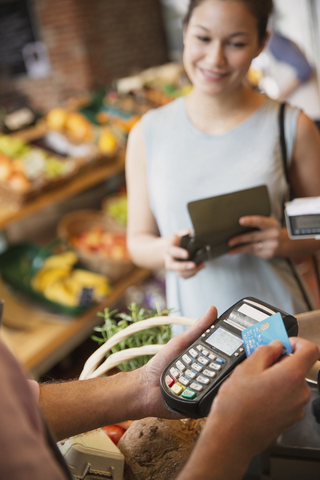Frau beobachtet Verkäuferin in einem Lebensmittelgeschäft bei der Benutzung eines Kreditkartenautomaten, lizenzfreies Stockfoto