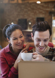 Lächelndes Paar trinkt Cappuccino am Laptop im Café - CAIF10411