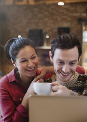 Smiling couple drinking cappuccino at laptop in cafe - CAIF10411