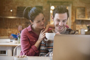 Smiling couple drinking coffee using laptop at cafe - CAIF10420