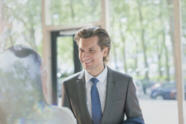 Smiling businessman talking to businesswoman in lobby - CAIF10440