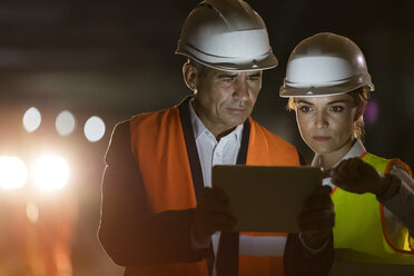 Bauarbeiter und Ingenieur mit digitalem Tablet auf einer dunklen Baustelle - CAIF10442