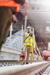 Männlicher Ingenieur mit Theodolit auf Gleisen auf einer Baustelle - CAIF10443