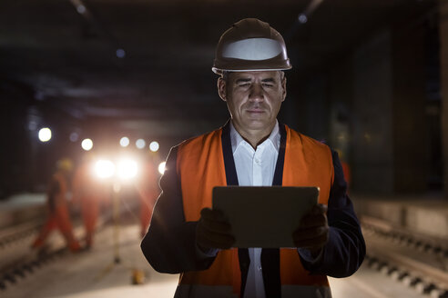 Seriöser männlicher Vorarbeiter, der ein digitales Tablet auf einer dunklen Baustelle benutzt - CAIF10445