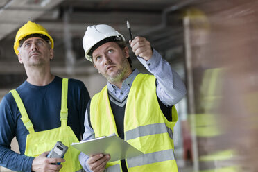 Male foreman and engineer with clipboard looking up at construction site - CAIF10450