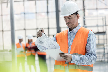 Male engineer reviewing blueprints on clipboard at construction site - CAIF10451