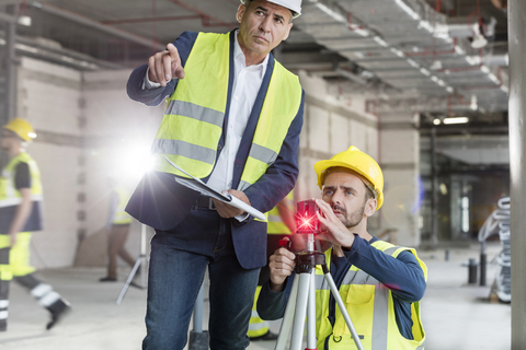 Männlicher Polier und Ingenieur mit Theodolit auf einer Baustelle, lizenzfreies Stockfoto