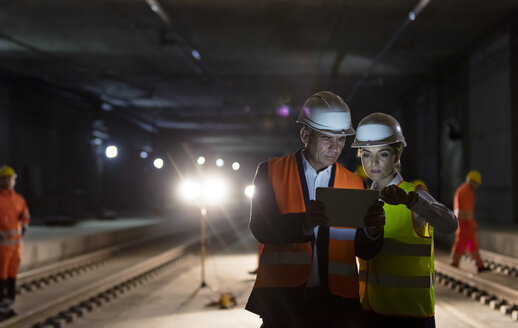 Vorarbeiter und Bauarbeiter verwenden ein digitales Tablet auf einer dunklen unterirdischen Baustelle - CAIF10459