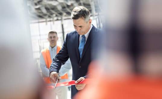 Geschäftsmann zerschneidet Band auf neuer Baustelle - CAIF10464