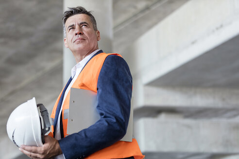 Seriöser Geschäftsmann mit Schutzhelm auf einer Baustelle - CAIF10467