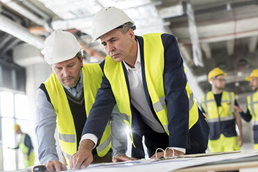 Männliche Ingenieure betrachten Baupläne auf einer Baustelle - CAIF10468
