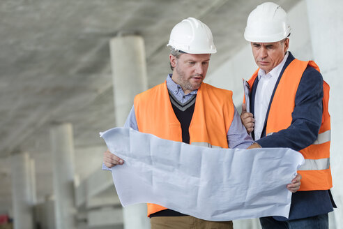 Männliche Ingenieure, die auf einer Baustelle unterirdische Baupläne prüfen - CAIF10469