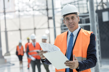 Portrait lächelnder Geschäftsmann mit Klemmbrett auf einer Baustelle - CAIF10472