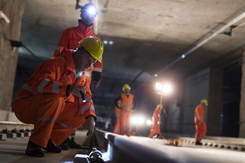 Männliche Bauarbeiter, die unterirdische Gleise auf einer dunklen Baustelle untersuchen - CAIF10474